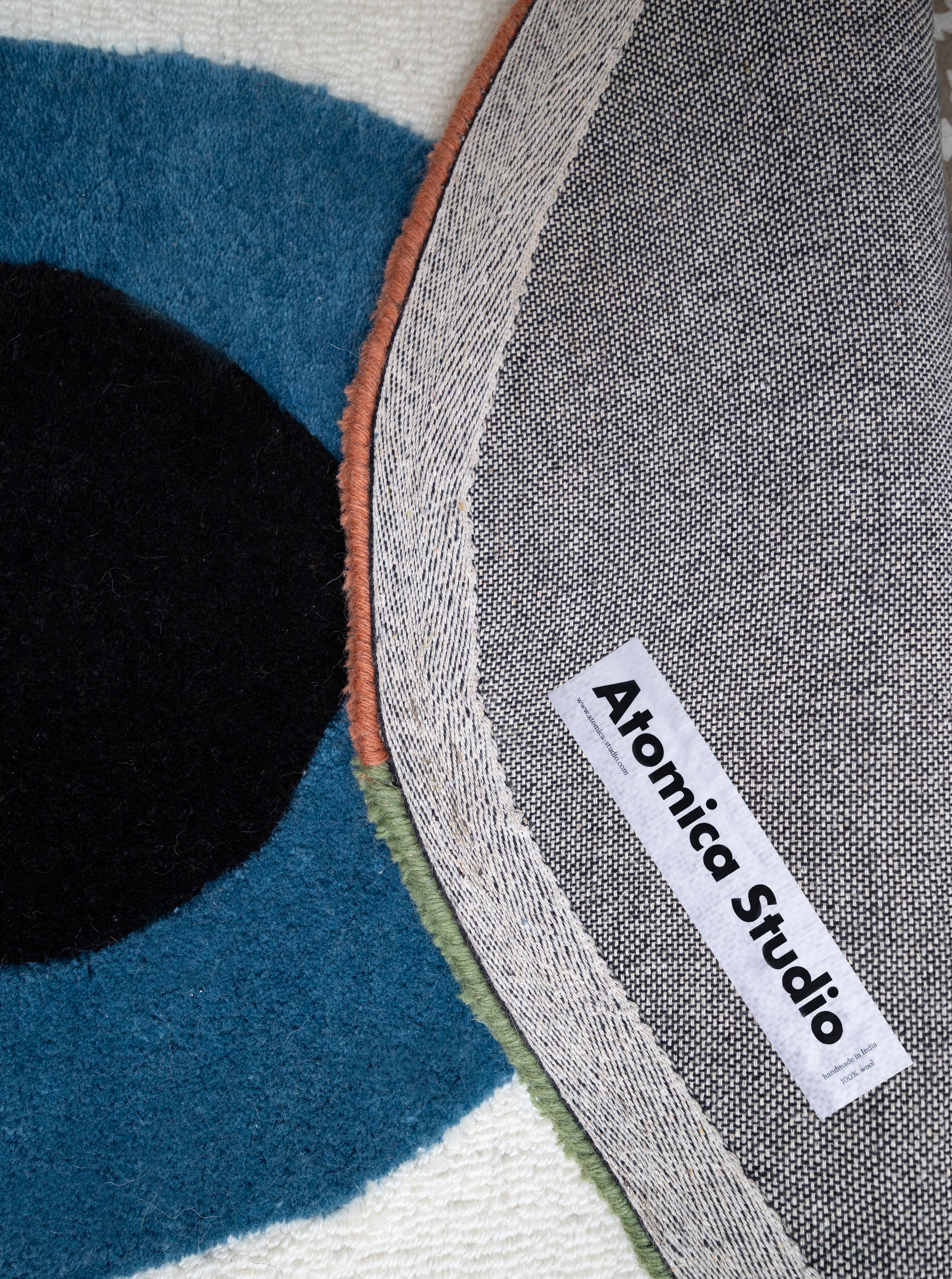 Primer plano de la alfombra Charm mostrando la etiqueta de la artista y la densidad de las fibras de lana en azul y negro.