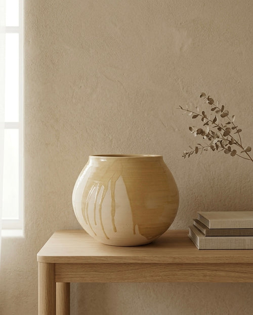 Vasija redonda tipo globo de cerámica de autor con acabado de esmalte brillante chorreado y base mate texturizada, expuesta en un ambiente decorativo minimalista y cálido.