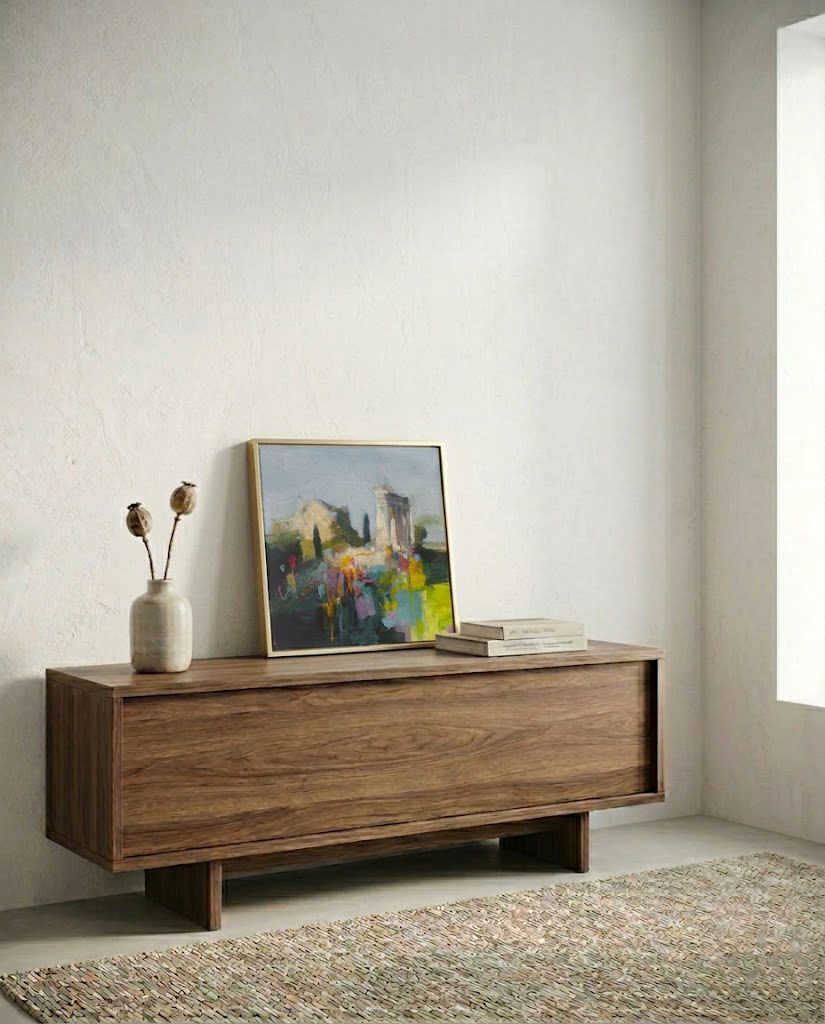 Cuadro abstracto enmarcado de la obra "El silencio antes del color" sobre un mueble aparador de madera en un salón moderno. La pintura, con tonos suaves y toques de amarillo y rosa fucsia, se muestra en una pared de yeso minimalista con luz natural. Fotografía de interiorismo contemporáneo.