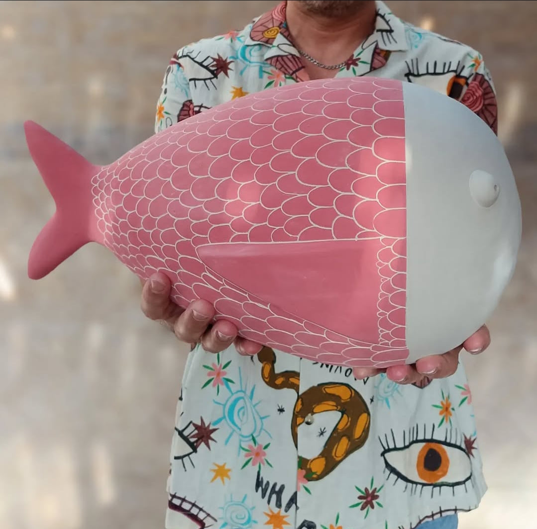 Primer plano de la escultura Pez XXL lisa en cerámica rosa pastel de Vicente Rivera, mostrada entre las manos de una persona con camisa estampada para referencia de su gran tamaño.