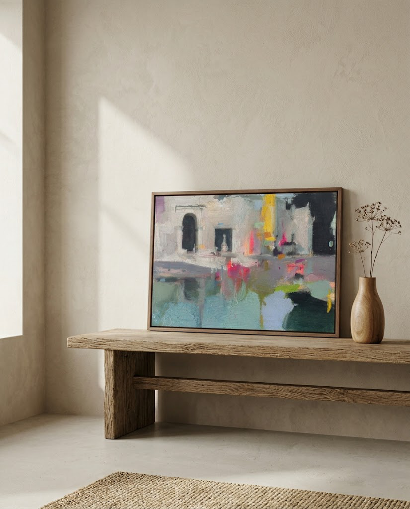 Cuadro enmarcado de la obra abstracta "Jardines de la Memoria" en un salón minimalista de estilo zen. La pintura, que evoca arquitectura mediterránea en tonos turquesa y fucsia, está sobre un banco de madera rústica junto a un jarrón con ramas secas. Fotografía de interiorismo con luz natural.