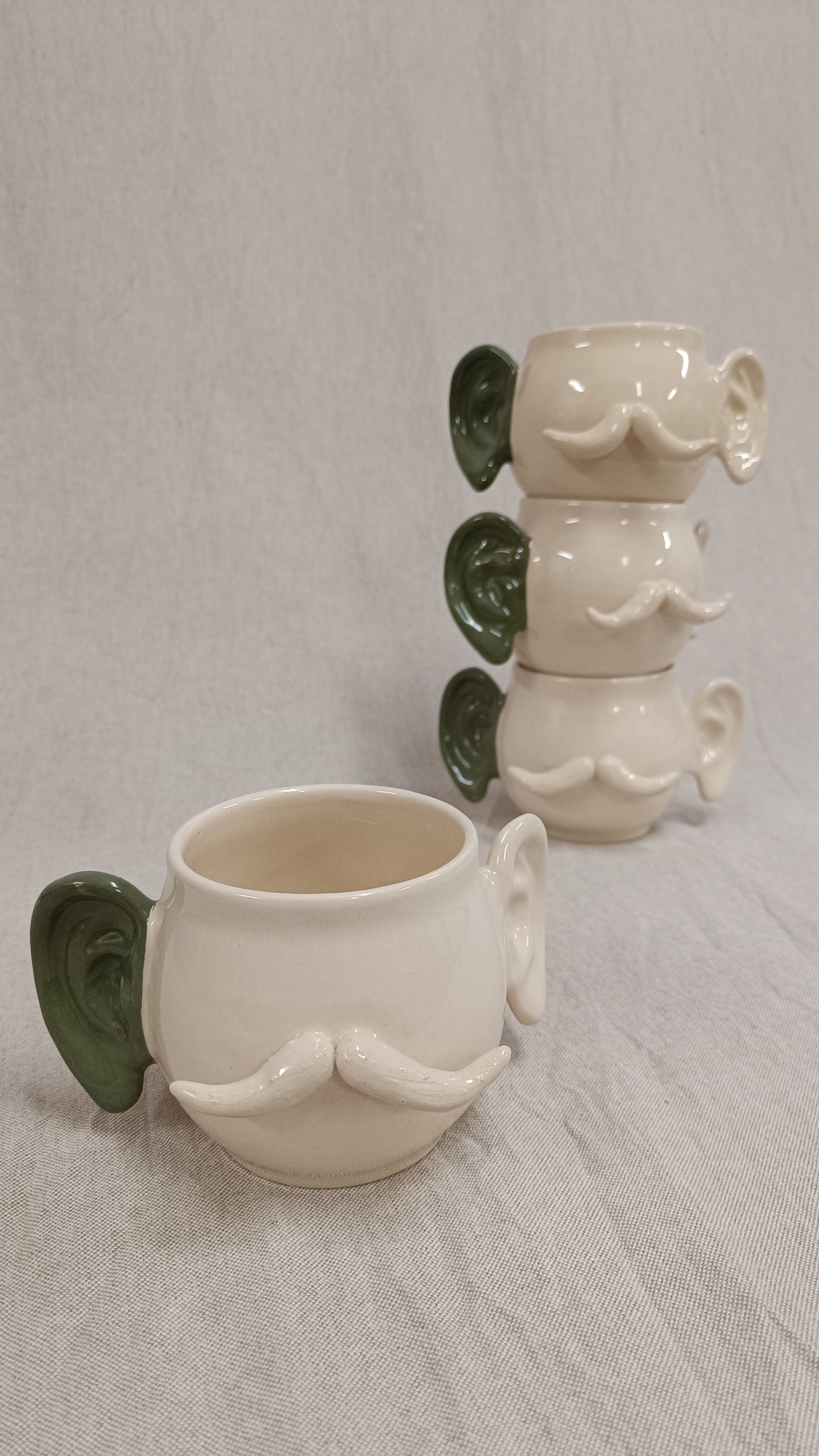 Taza hombre oreja verde de Vicente Rivera en primer plano con una torre de tres tazas idénticas apiladas detrás sobre fondo neutro