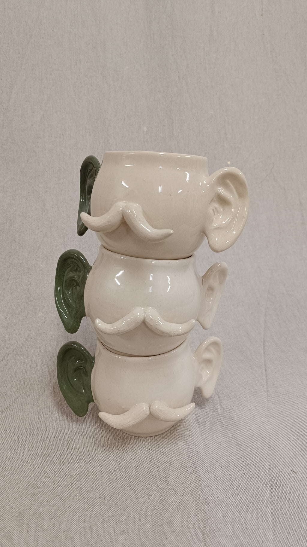 Plano medio de tres tazas de cerámica apiladas verticalmente mostrando las orejas verdes alineadas en el lado izquierdo.