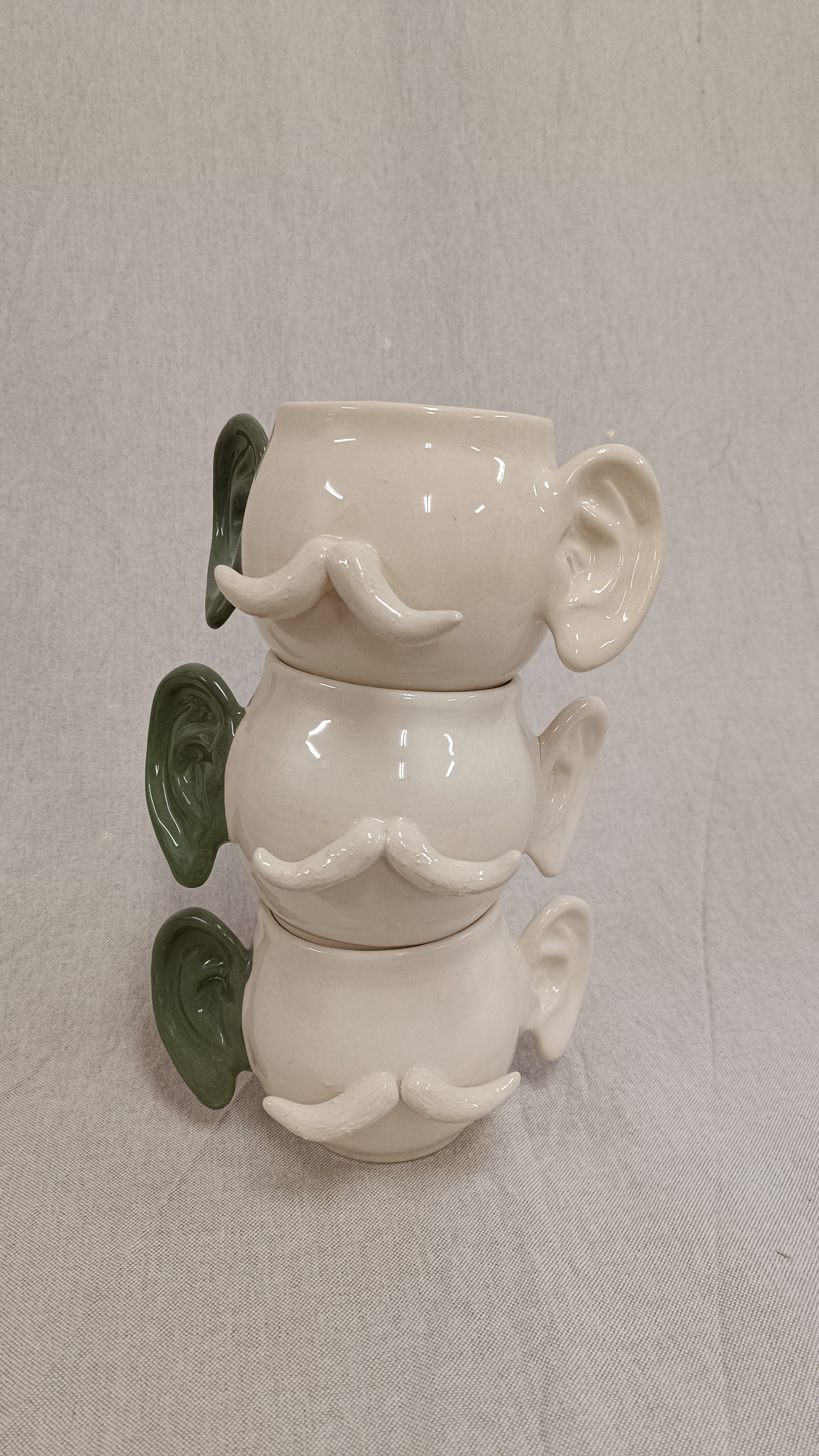 Plano medio de tres tazas de cerámica apiladas verticalmente mostrando las orejas verdes alineadas en el lado izquierdo.