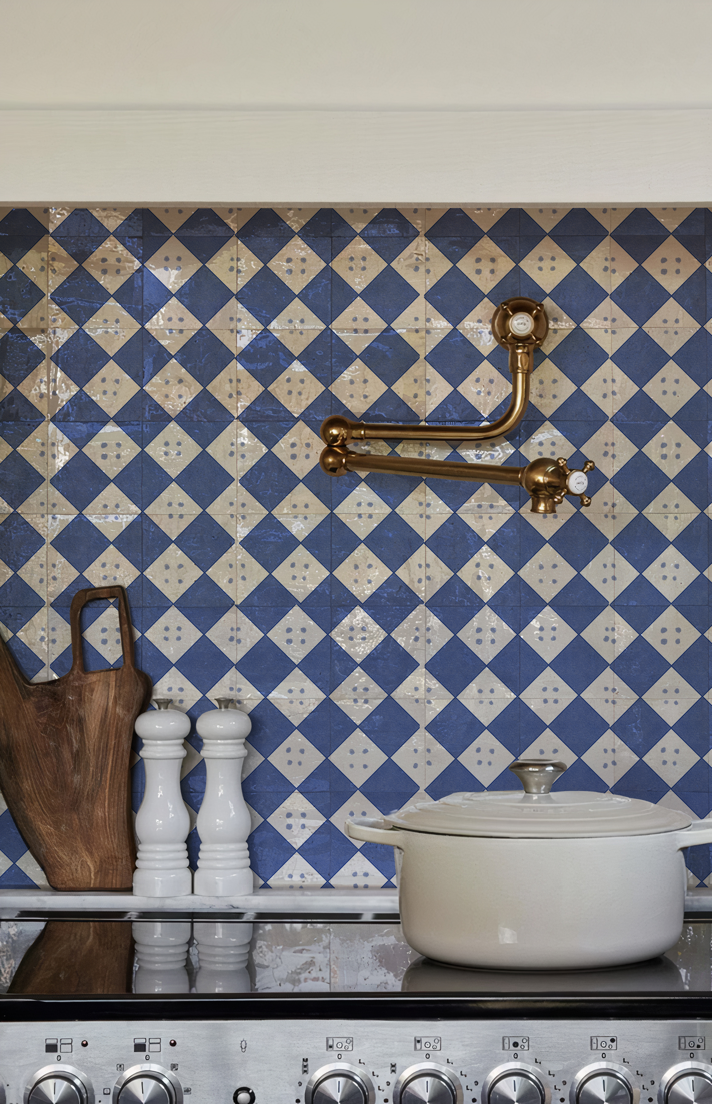 Ambiente de cocina de alta gama con grifería pot filler de cobre, olla de hierro fundido y el Azulejo Diamante en bruto con patrón geométrico azul instalado en el frente de cocción.