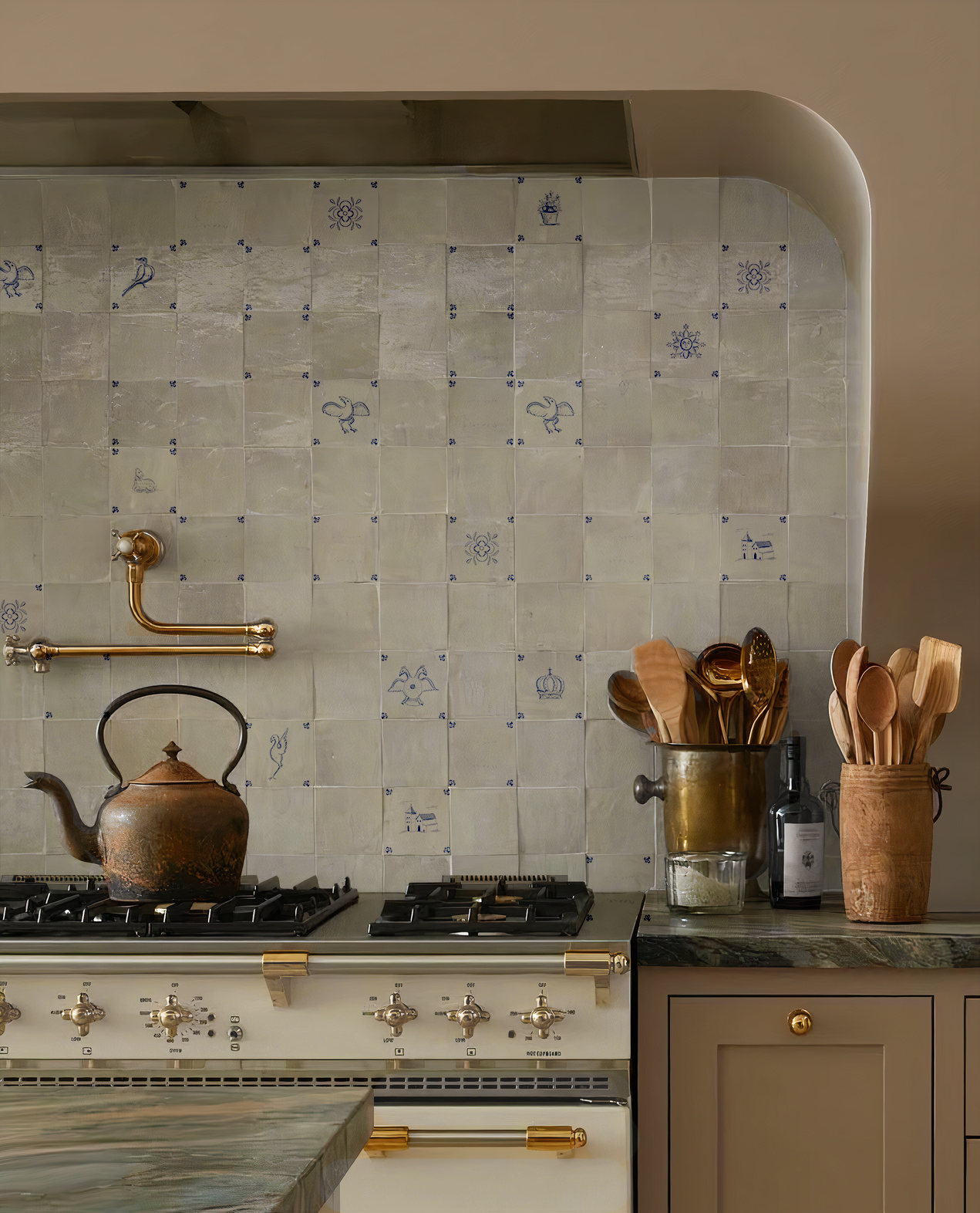 Vista de una cocina de lujo con un frente revestido de azulejos blancos esmaltados, que presentan sutiles dibujos azules de pájaros y escudos, situados sobre una cocina de gas de color crema y accesorios de cocina de cobre y madera.