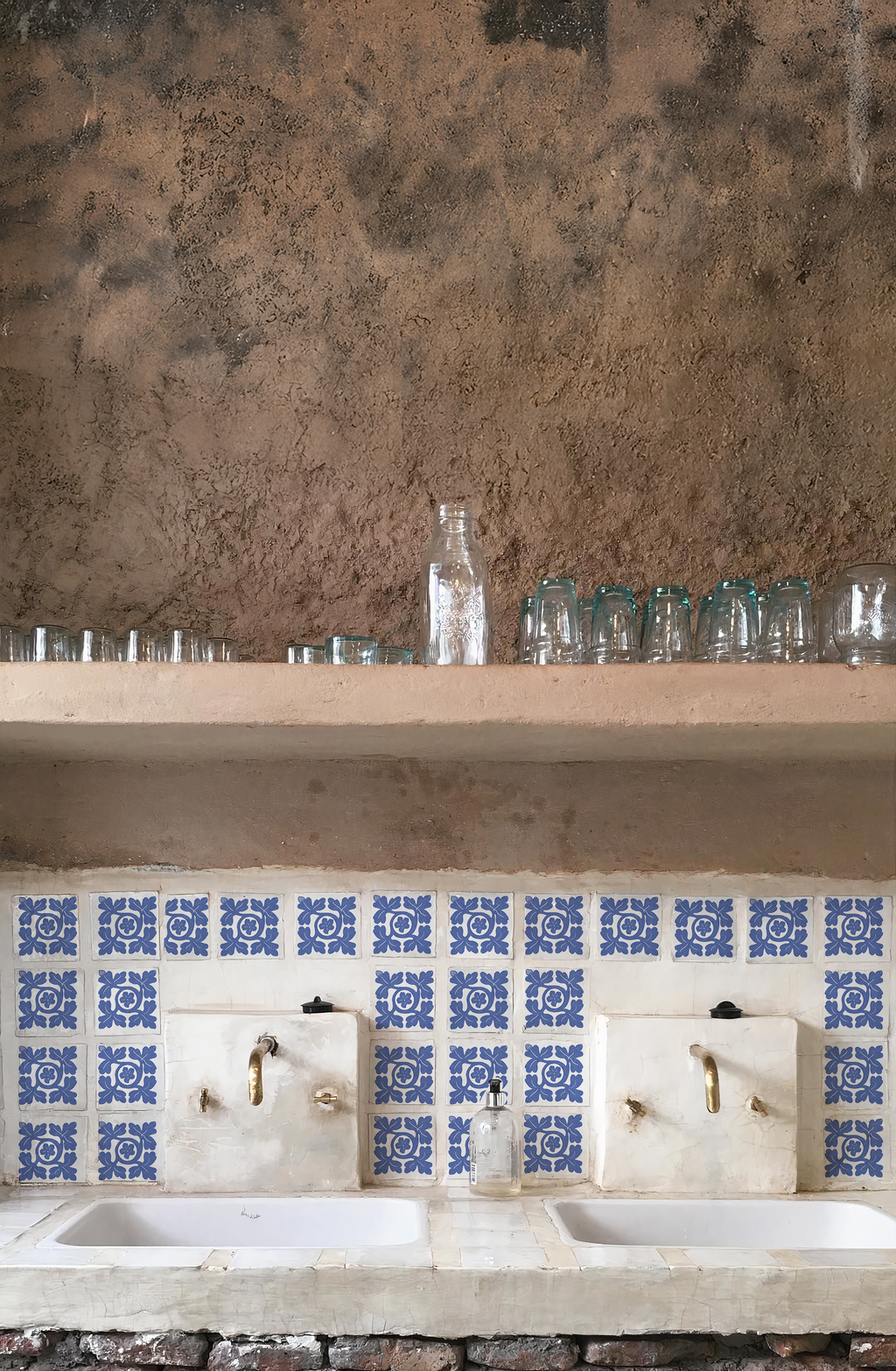 Vista frontal de una estación de lavado doble de estilo rústico y andino con dos lavabos blancos, grifería de latón envejecido y un frente revestido con el Azulejo Diamante en bruto.