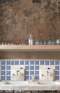 Vista frontal de una estación de lavado doble de estilo rústico y andino con dos lavabos blancos, grifería de latón envejecido y un frente revestido con el Azulejo Diamante en bruto.