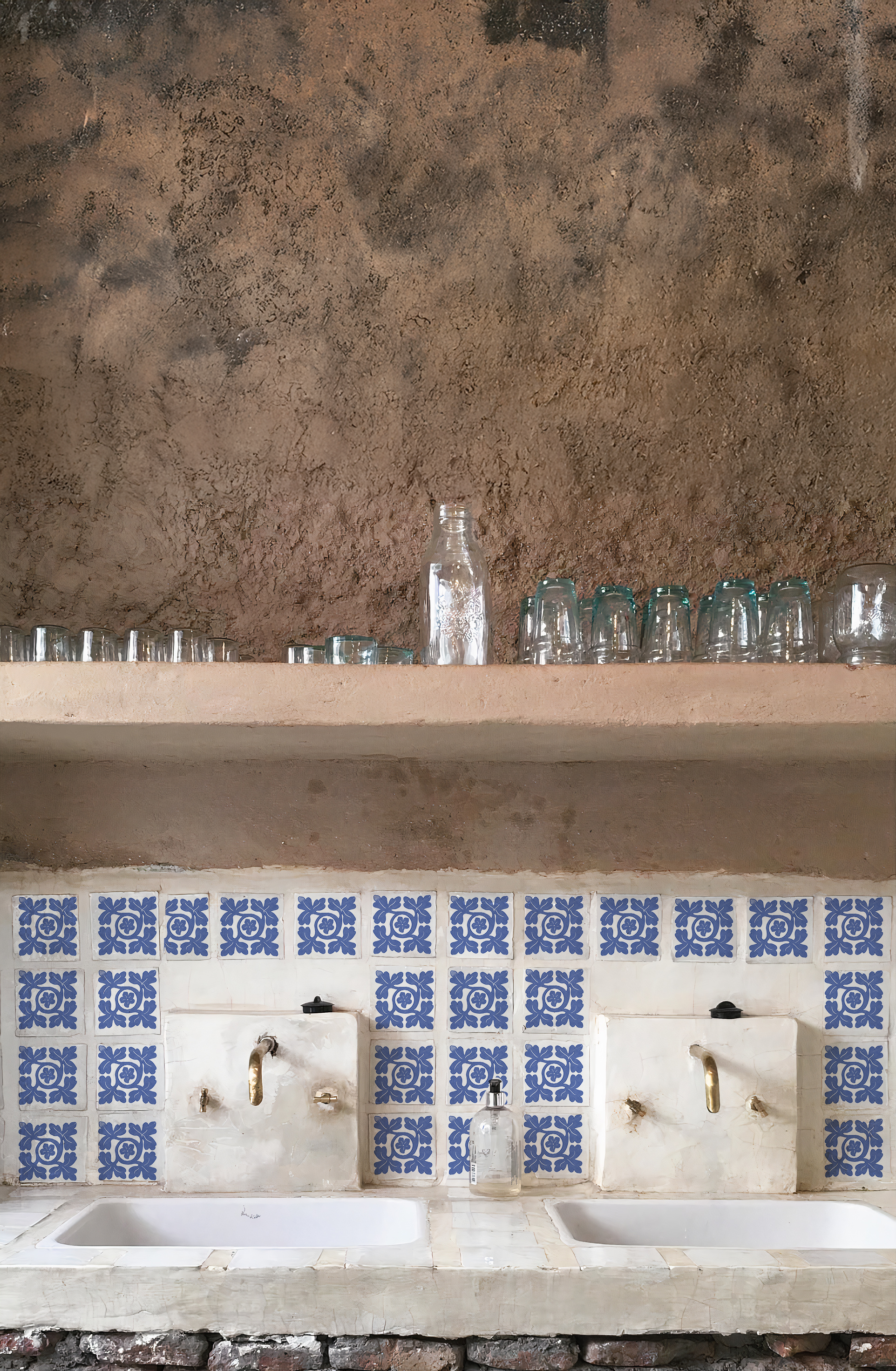 Vista frontal de una estación de lavado doble de estilo rústico y andino con dos lavabos blancos, grifería de latón envejecido y un frente revestido con el Azulejo Diamante en bruto.