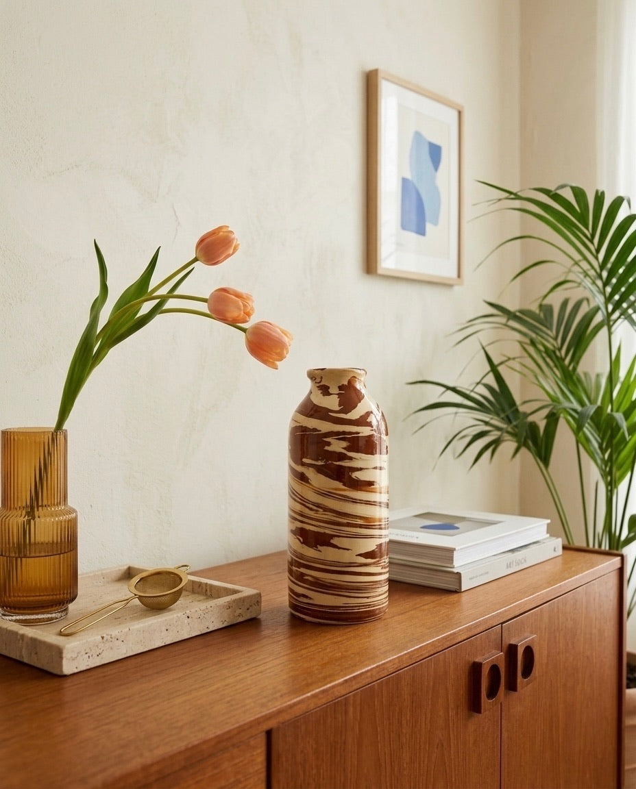Botella de cerámica jaspeada TerraLith de Cecilia Behrend sobre un aparador de madera, integrada en una decoración cálida con tulipanes y plantas de interior.