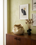 Jarrón artesanal Calima Fuentón 1 de Cecilia Behrend sobre cómoda de madera, decoración minimalista con pared verde suave.