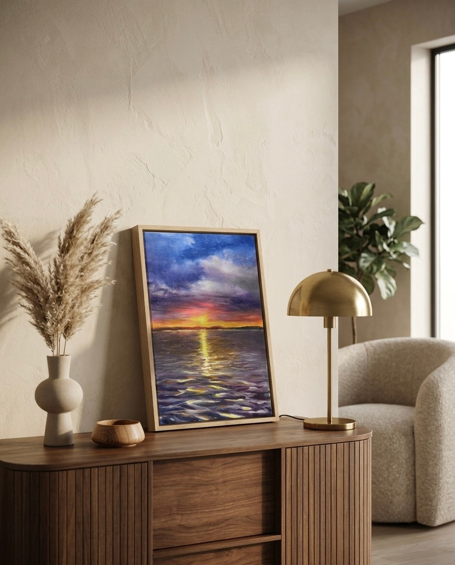 Primer plano de la pintura al óleo de atardecer, "Destellos en el mar", enmarcada en madera natural y colocada sobre un aparador moderno de listones junto a una lámpara dorada y pampas grass, reflejando el estilo de Sezme Decor.