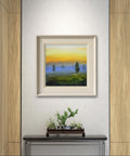 Simulación decorativa de la obra "Amanecer y niebla" enmarcada en una pared minimalista sobre un mueble con un bonsái.