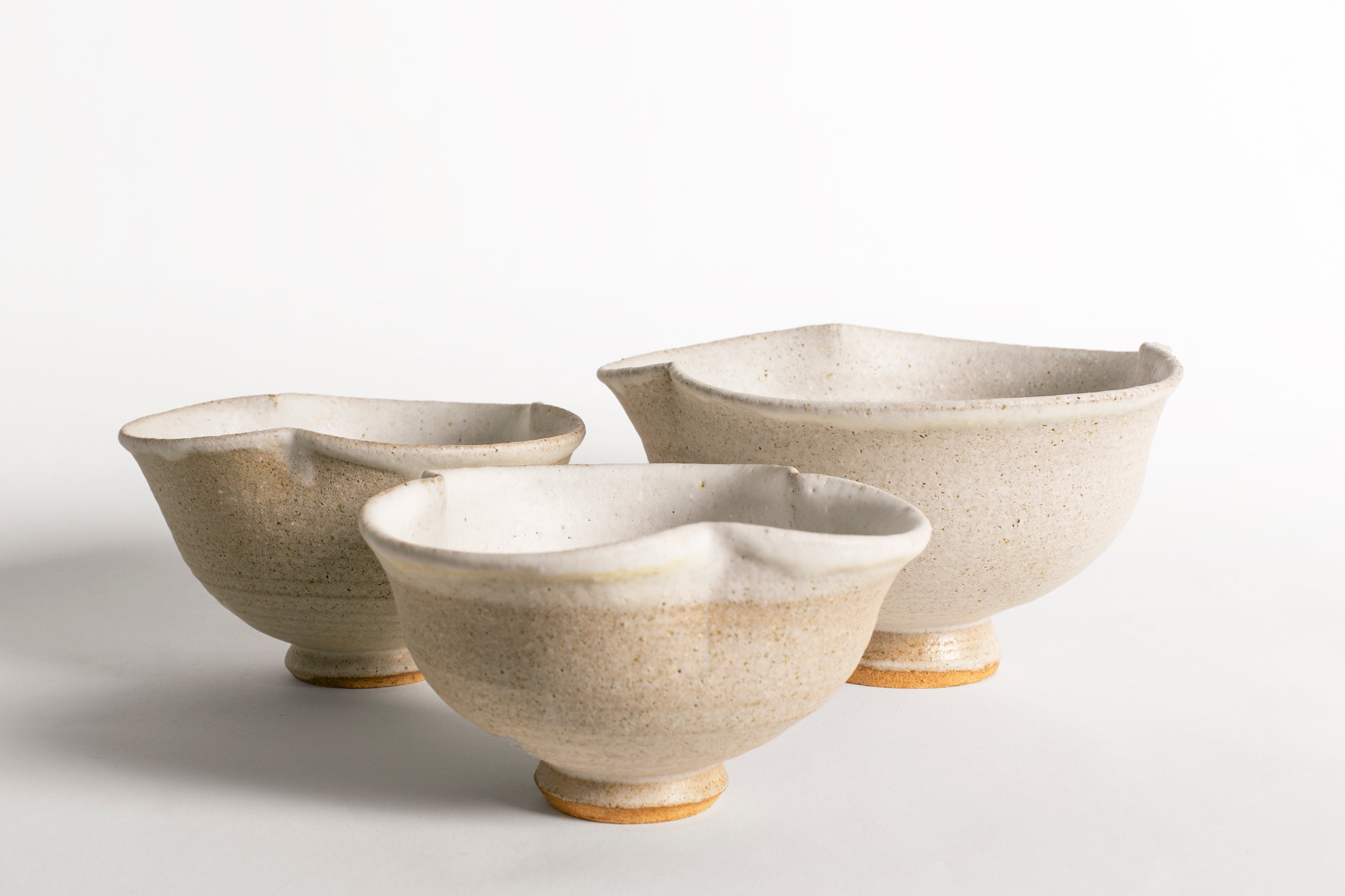 Conjunto de tres cuencos de cerámica artesanal en tonos blanco roto y arena con formas orgánicas.