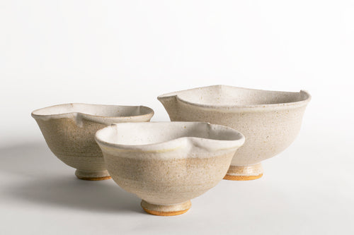 Conjunto de tres cuencos de cerámica artesanal en tonos blanco roto y arena con formas orgánicas.