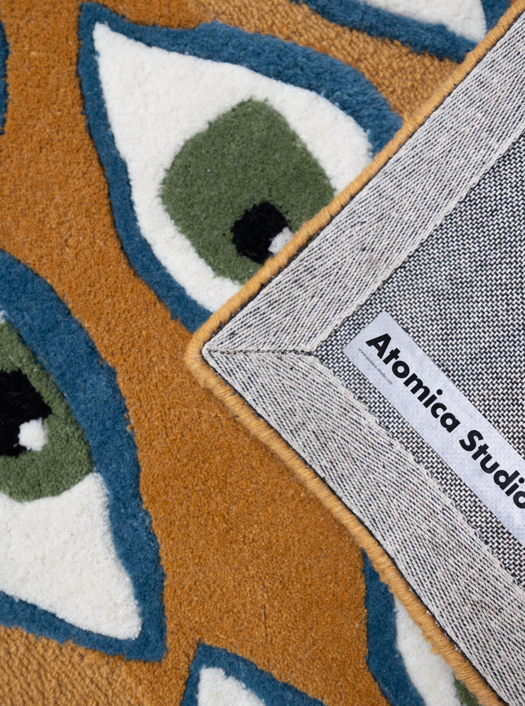 Detalle del tejido de alta densidad de la alfombra Amuleto, mostrando la textura de las fibras y la etiqueta de autoría en el reverso.