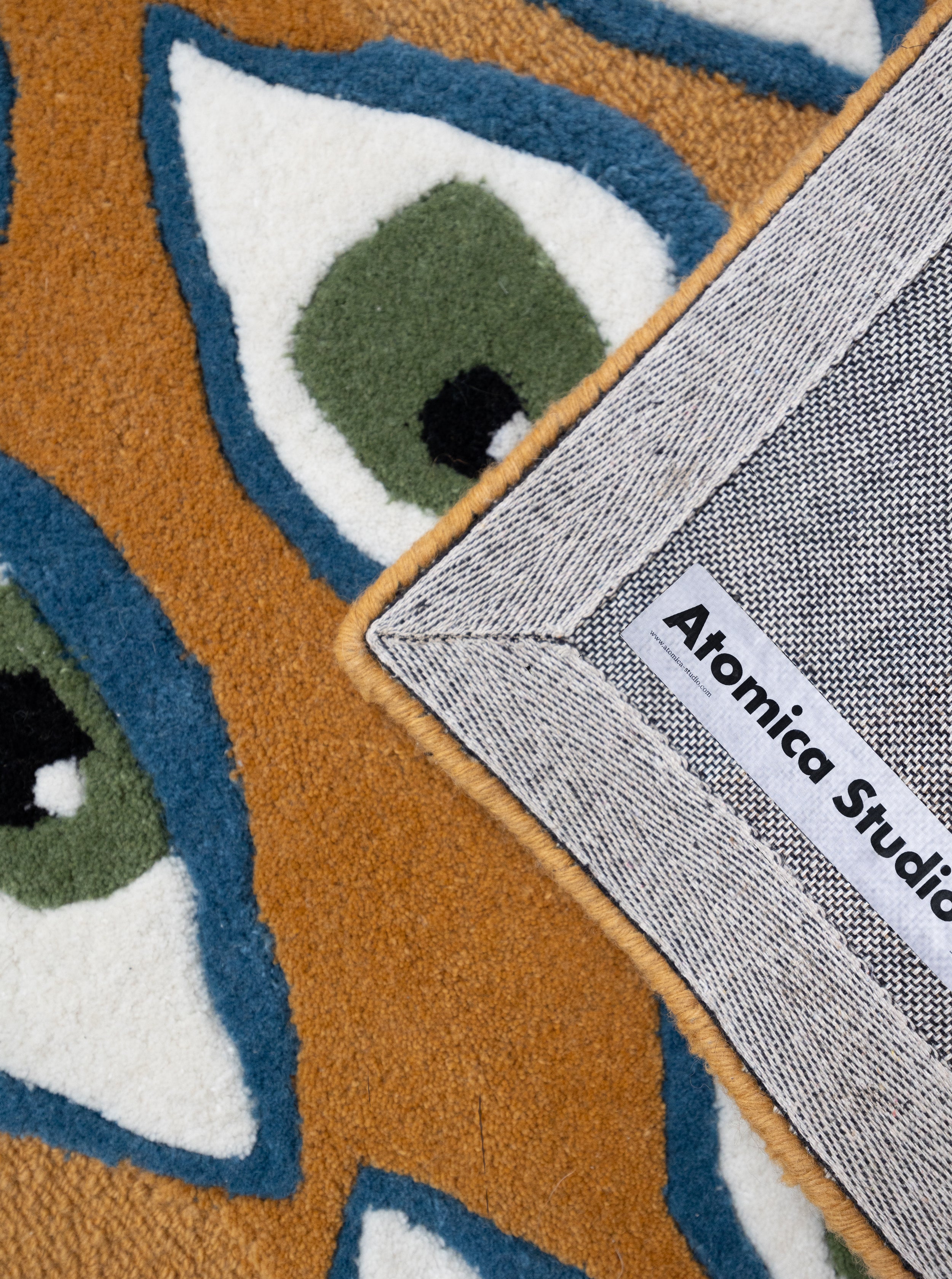 Detalle del tejido de alta densidad de la alfombra Amuleto, mostrando la textura de las fibras y la etiqueta de autoría en el reverso.