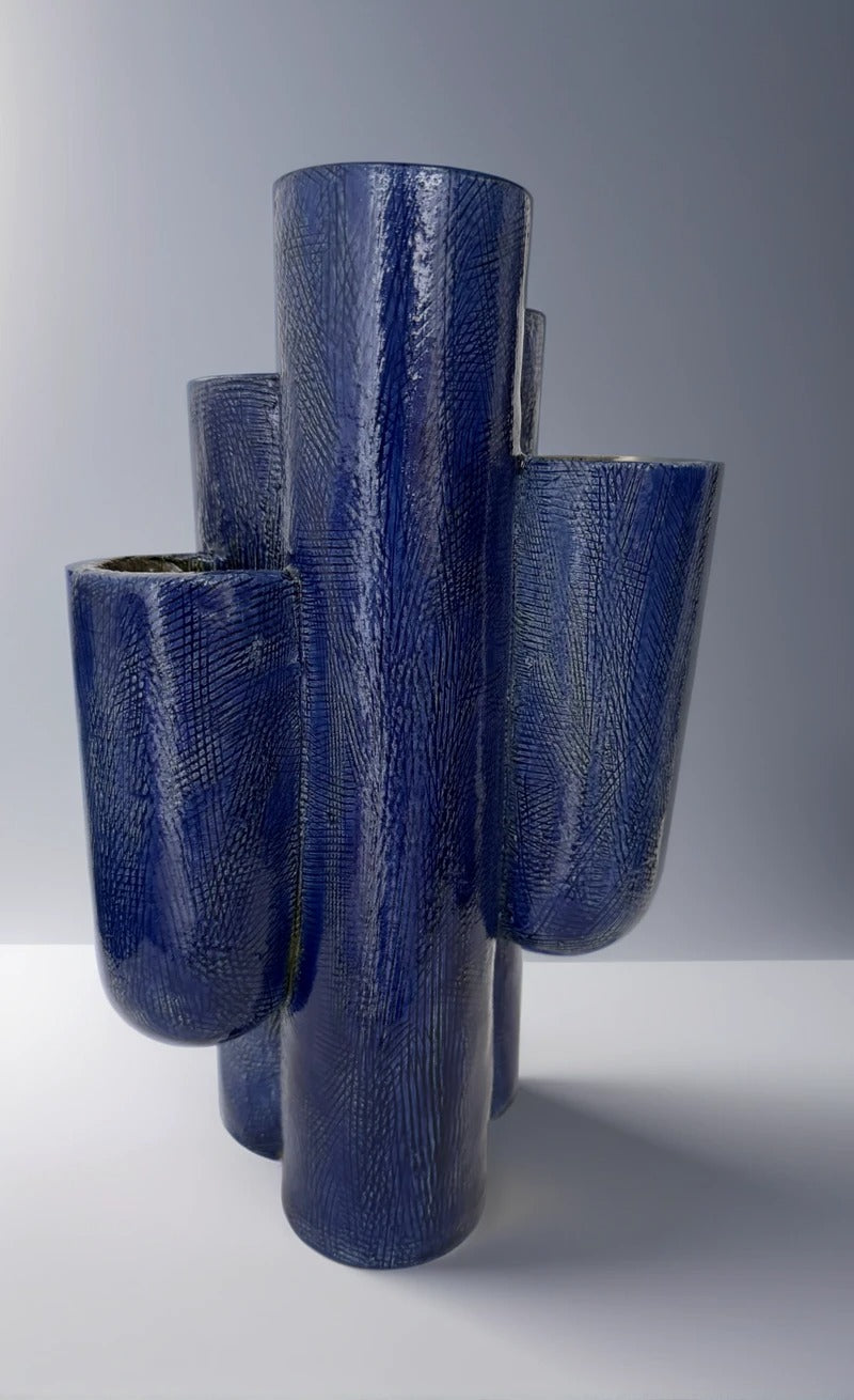 Vista frontal de la escultura "ENCUENTRO" de Fernanda Salomé, mostrando sus múltiples cilindros de cerámica en azul cobalto sobre fondo neutro.
