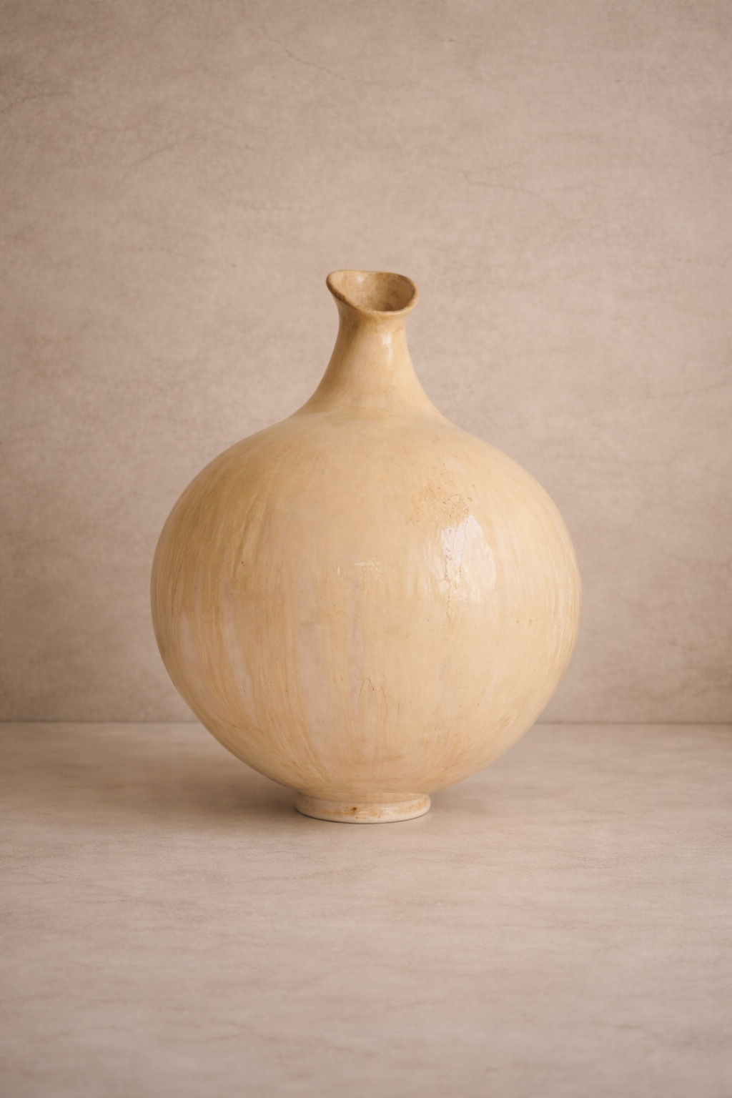 Escultura de cerámica artesanal Sfera 2 con cuerpo circular, cuello largo y embocadura oblicua en tono crema satinado.