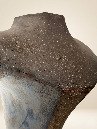 Plano medio superior de la escultura que acentúa la textura granulada del gres y la transición del marrón oscuro al azul iridiscente metálico en la base de Fernanda Salomé.