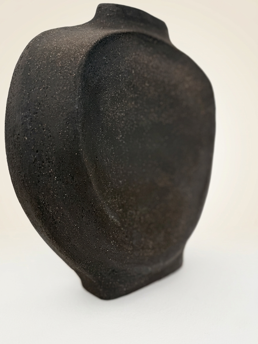 Primer plano lateral de la escultura "GESTO" de Fernanda Salomé en gres negro carbón, resaltando la esbeltez de su perfil de 7 cm y la interacción de la luz sobre la textura rugosa sobre fondo neutro.