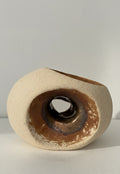 Escultura minimalista de gres "HALO" de Fernanda Salomé, con exterior texturizado crema mate y cavidad interna circular con esmalte reactivo bronce brillante, sobre fondo neutro.