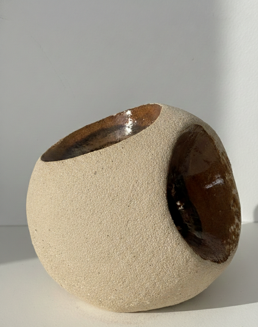 Escultura minimalista de gres "HALO" de Fernanda Salomé, mostrando su forma compleja asimétrica con múltiples oquedades elípticas de esmalte reactivo bronce brillante, sobre fondo neutro.
