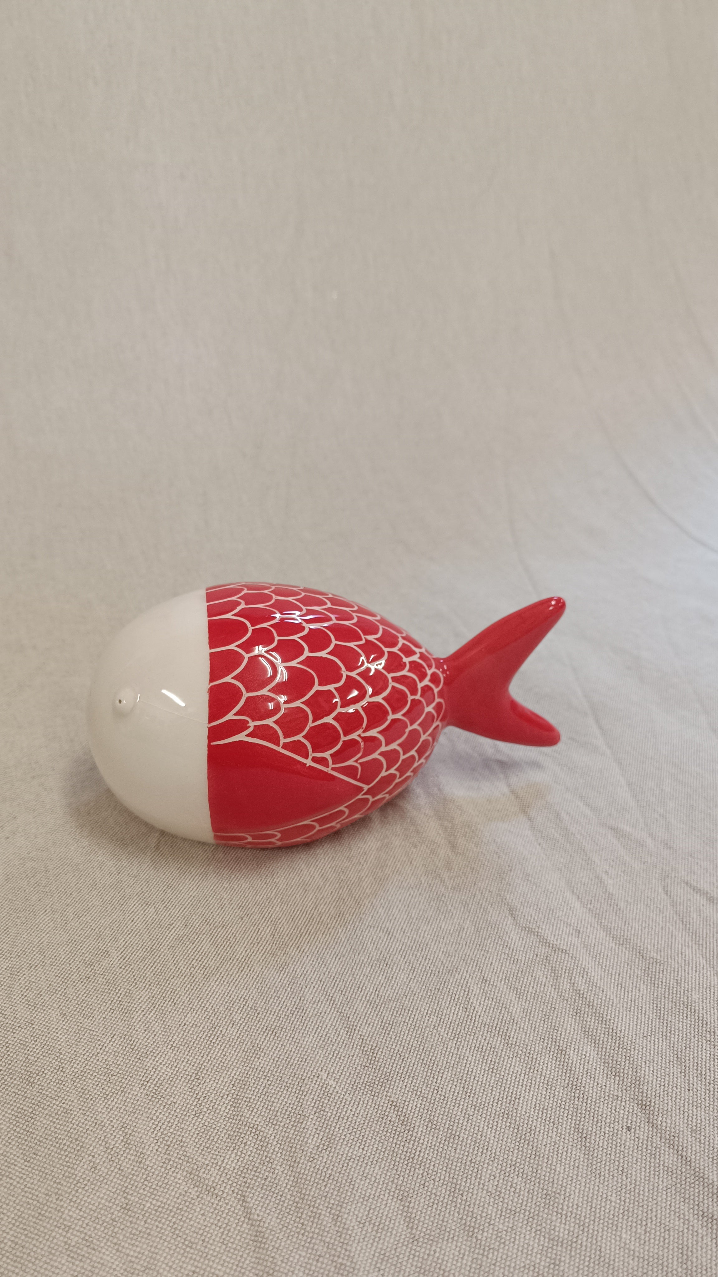 Primer plano de una escultura de pez en gres rojo con un patrón detallado de escamas blancas perfiladas a mano por el artista Vicente Rivera.