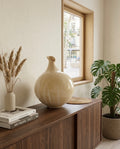 Escultura de cerámica Sfera de Cecilia Behrend para Sezme Decor, colocada sobre un aparador de madera oscura en un salón de diseño minimalista junto a una planta Monstera y libros de arte.