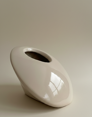 Jarrón escultórico de cerámica esmaltada "ELIPSE" de Fernanda Salomé, con forma asimétrica inclinada y acabado crema vetado, decorado con una flor blanca sobre fondo neutro.