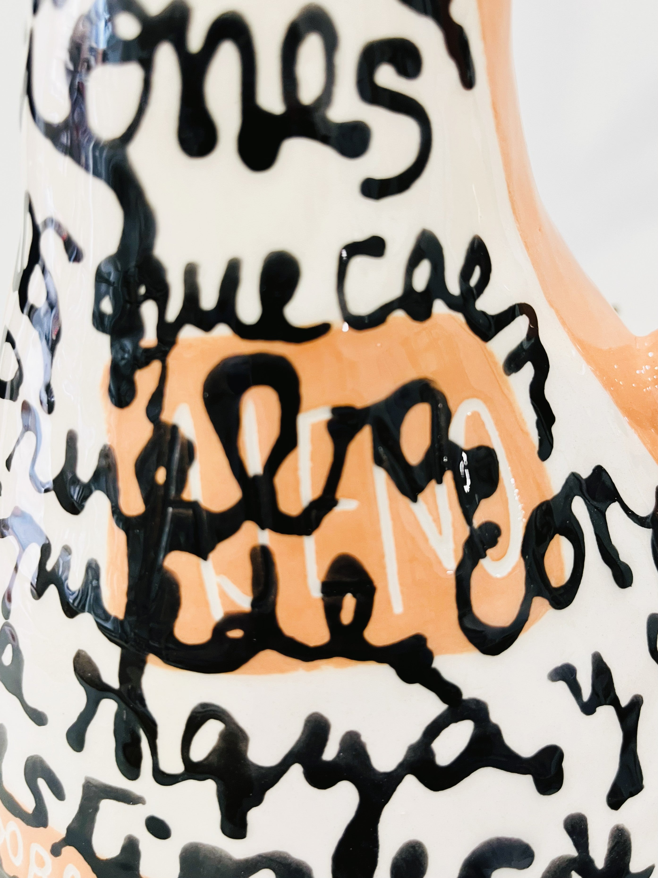 Jarrón IRRESUELTA cerámico expuesto frente a una pared con caligrafía artística, mostrando su escala y presencia decorativa.