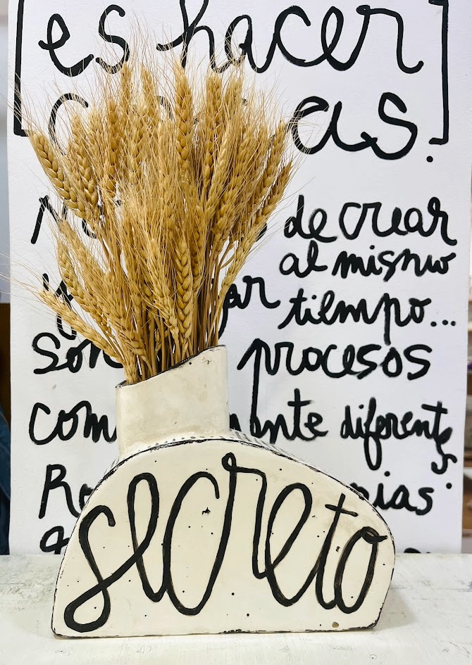 Jarrón SORPRESA cerámico expuesto frente a una pared con caligrafía artística, mostrando su escala y presencia decorativa.
