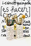 Vista frontal del Jarrón TINTA cerámico con asas amarillo ocre, mostrando su forma cilíndrica con boca ondulada y caligrafía expresionista en negro cobalto.