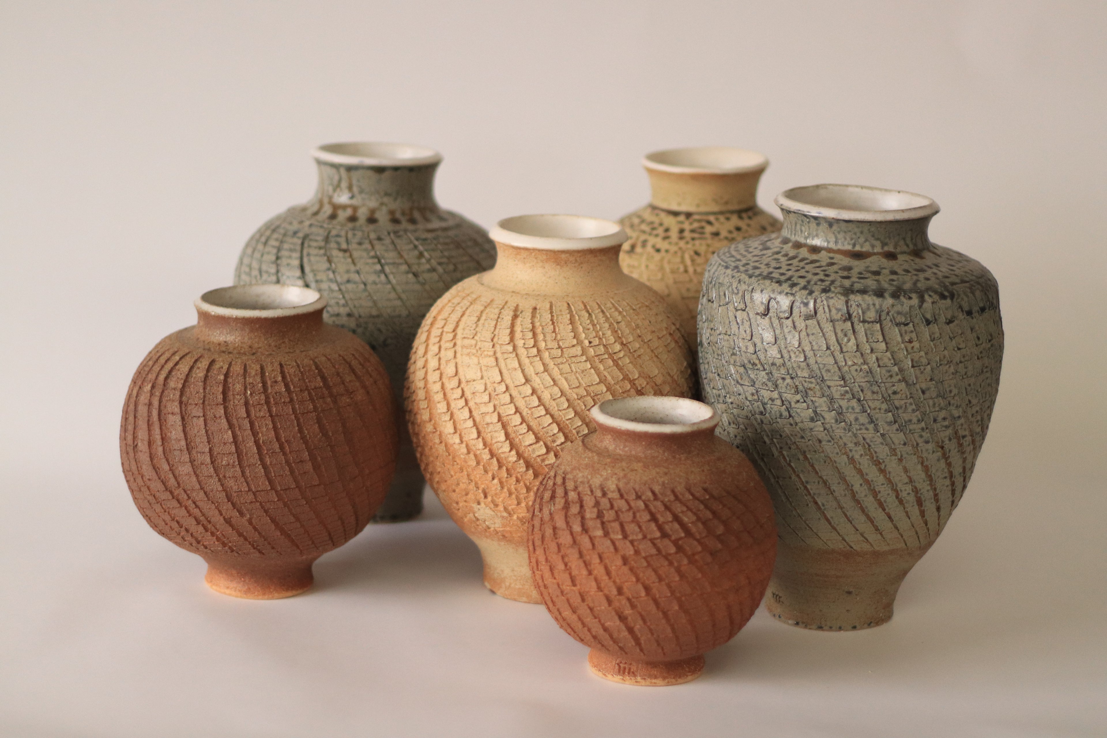 Colección de seis jarrones de cerámica artesanal "Pino" en diferentes tamaños y tonos tierra, con texturas geométricas grabadas a mano.