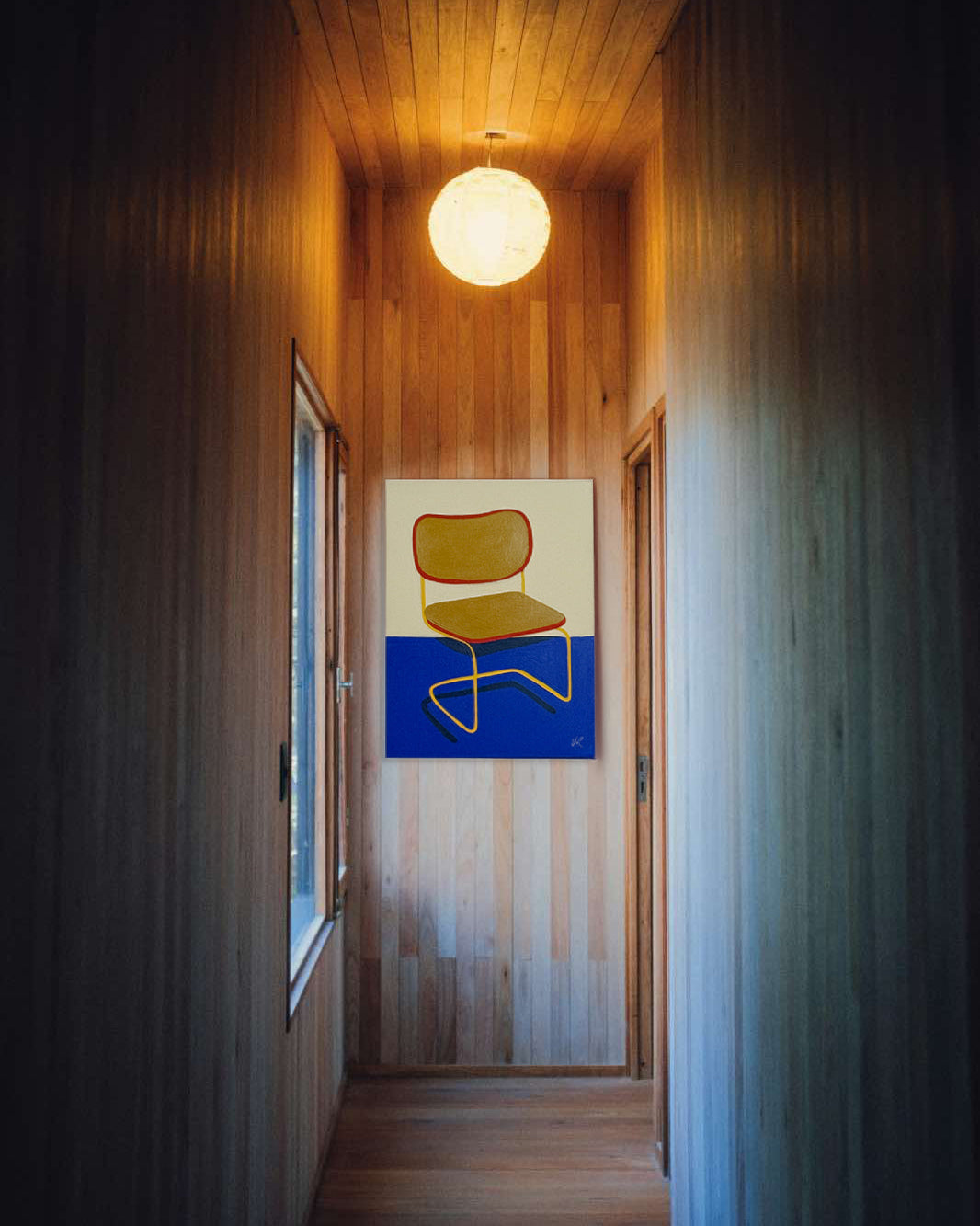 Obra "Esperando a Nadie" integrada en un rincón de lectura minimalista con una silla de diseño, mostrando su gran formato.