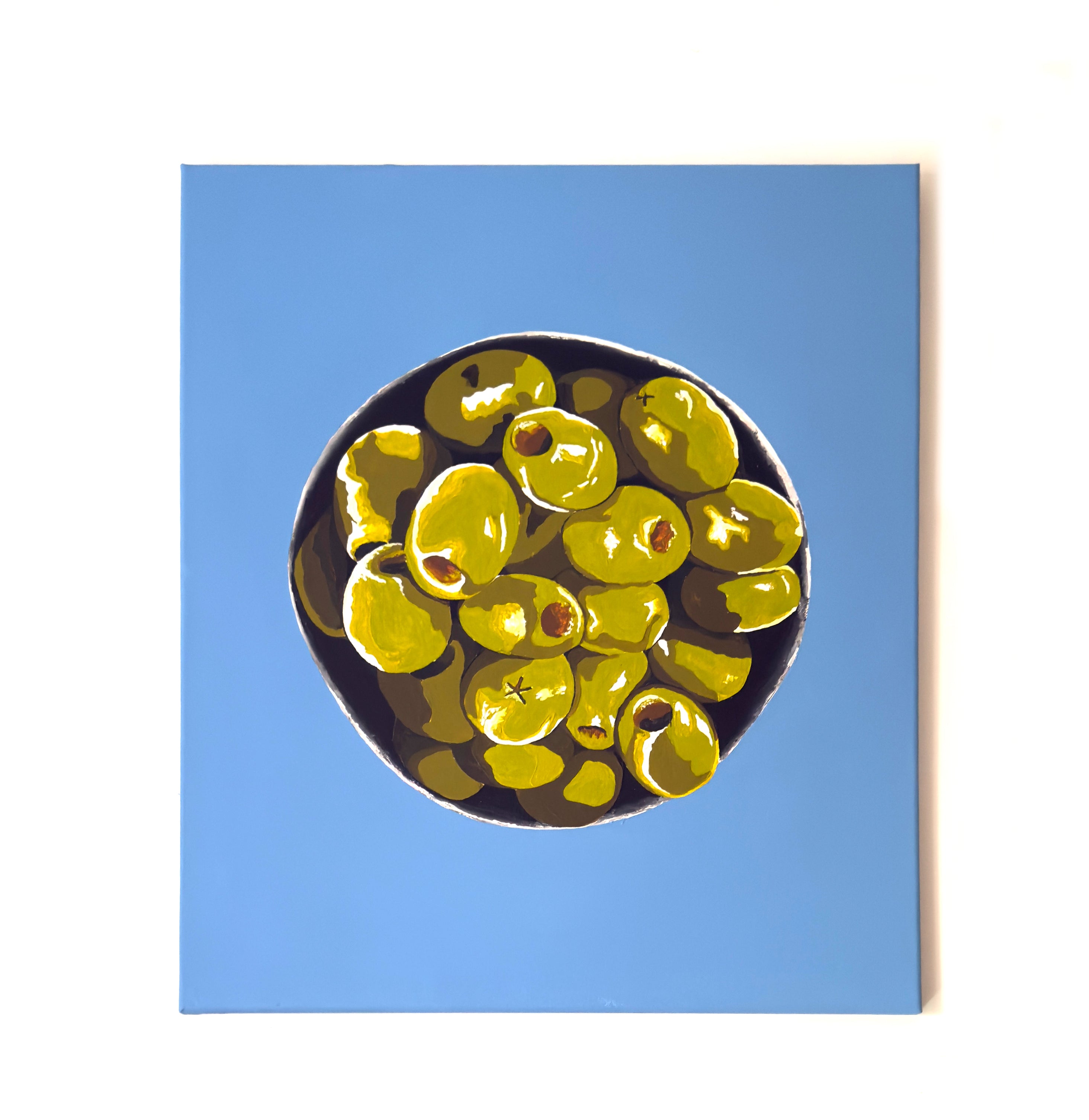Pintura de Valeria Moguel titulada "Oro Verde" que muestra un cuenco de aceitunas verdes sobre un fondo azul vibrante