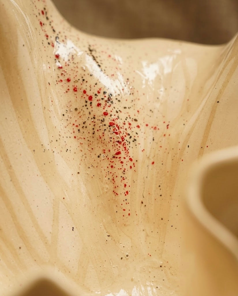 Detalle en primer plano del esmalte reactivo de la escultura de cerámica Flor Calima grande, mostrando las vetas fluidas de la arcilla y un salpicado fino en tonos rojos y negros.