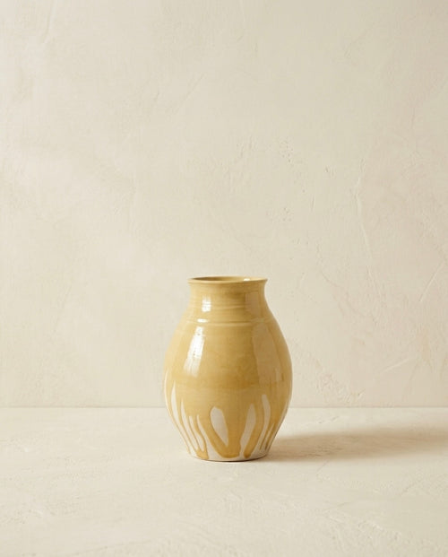 Vasija escultórica de cerámica de autor con acabado brillante en tono ocre y base texturizada con formas orgánicas fluidas, fotografiada sobre un fondo neutro minimalista.