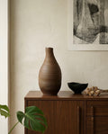 Vasija artesanal TerraLith Dark de Cecilia Behrend sobre aparador de madera, decoración de interiores minimalista.
