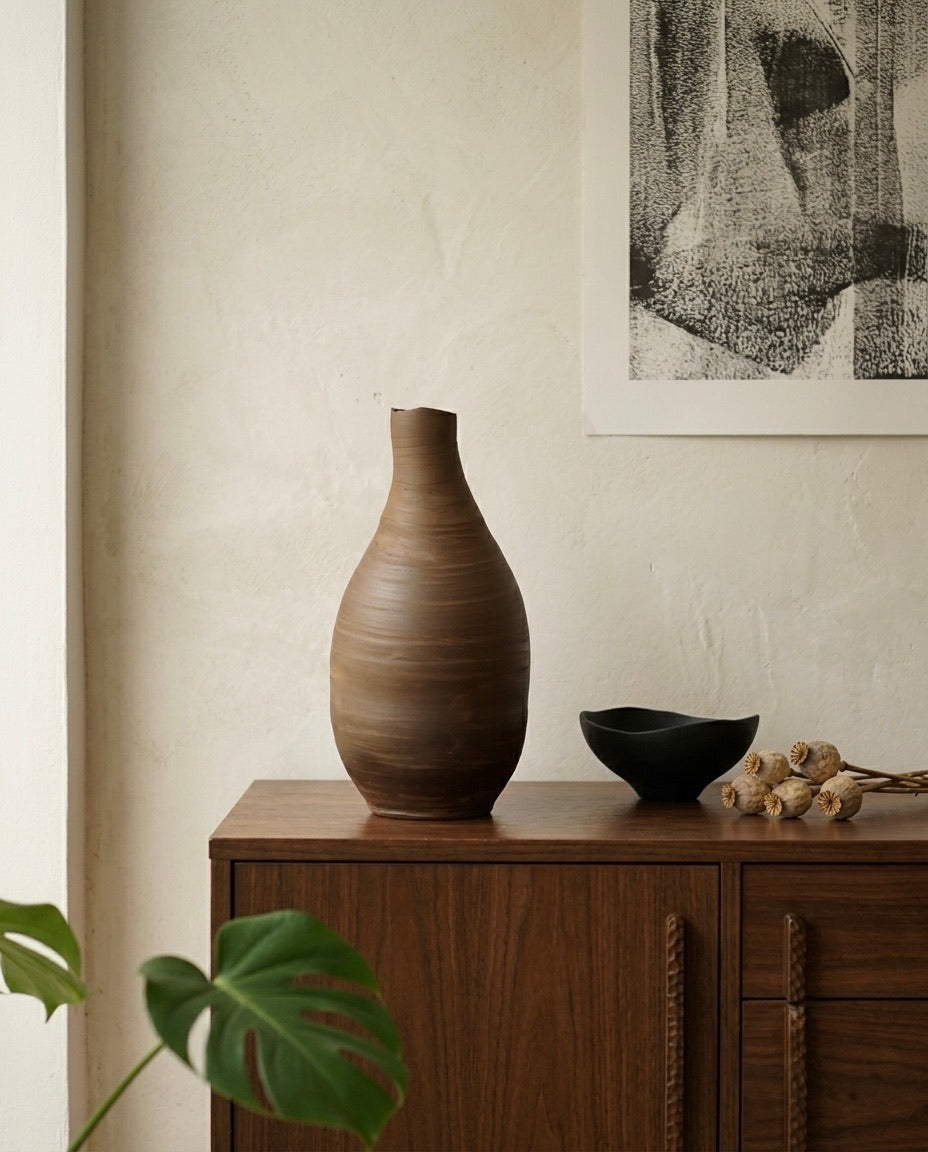 Vasija artesanal TerraLith Dark de Cecilia Behrend sobre aparador de madera, decoración de interiores minimalista.